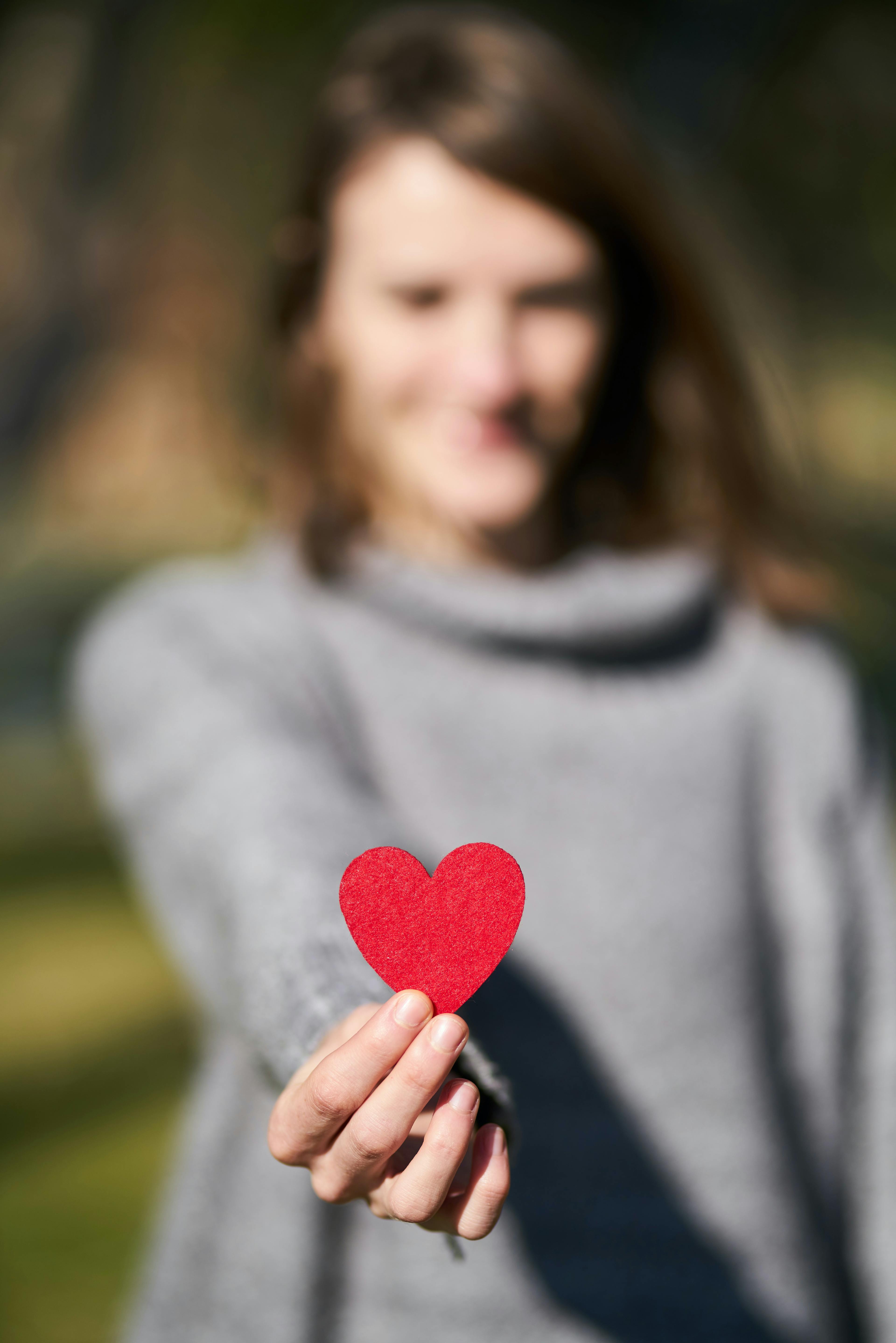 A woman holding a red peace of paper in the shape of a heart